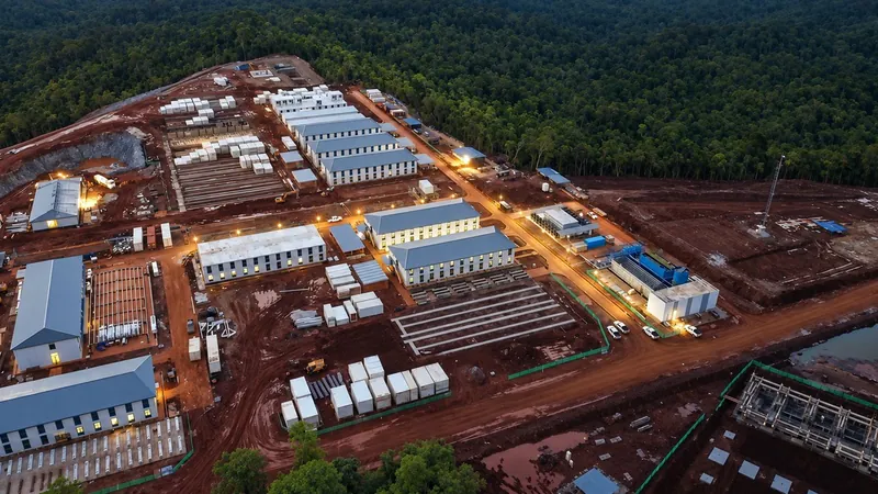 Aerial view of modular buildings on cleared red earth, with tropical forest behind